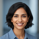 Smiling portrait of a South Asian woman, mid-30s, with short dark hair, against a soft blue and gray background.